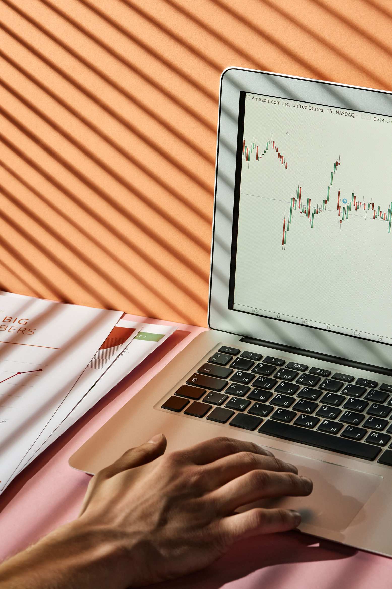 Hands typing on a keyboard with a cost-tracking spreadsheet on screen — Hand using a laptop with stock market graph, representing financial analysis.